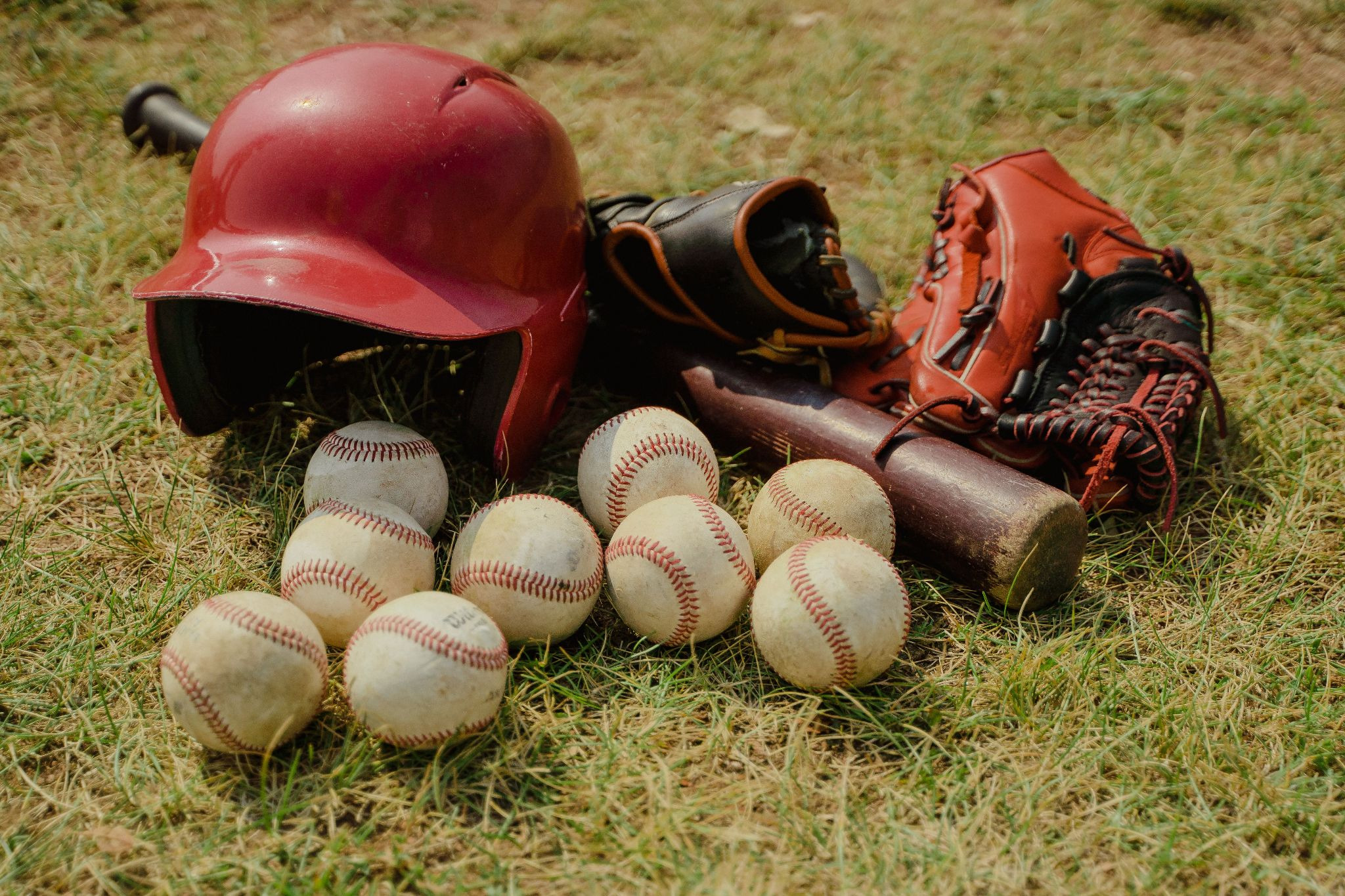 Baseball equipment on grass, mitts, a bat several balls and a batting helmet