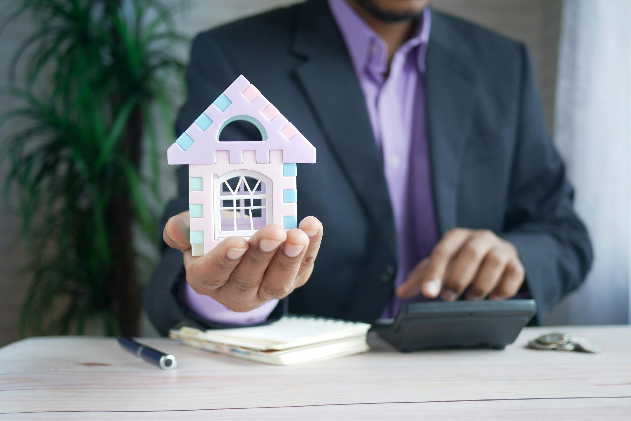 Property Manager holding a foam model house with their right hand and using a calculator with their left hand