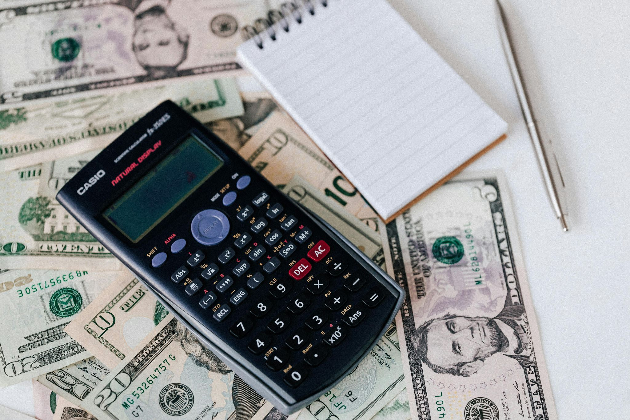 Calculator and notepad placed on a stack of USA dollars
